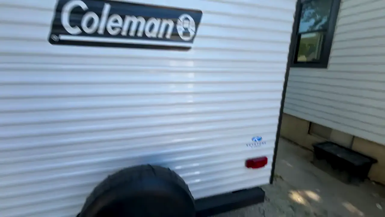 The rear of a Coleman travel trailer with a covered spare tire mounted on the back