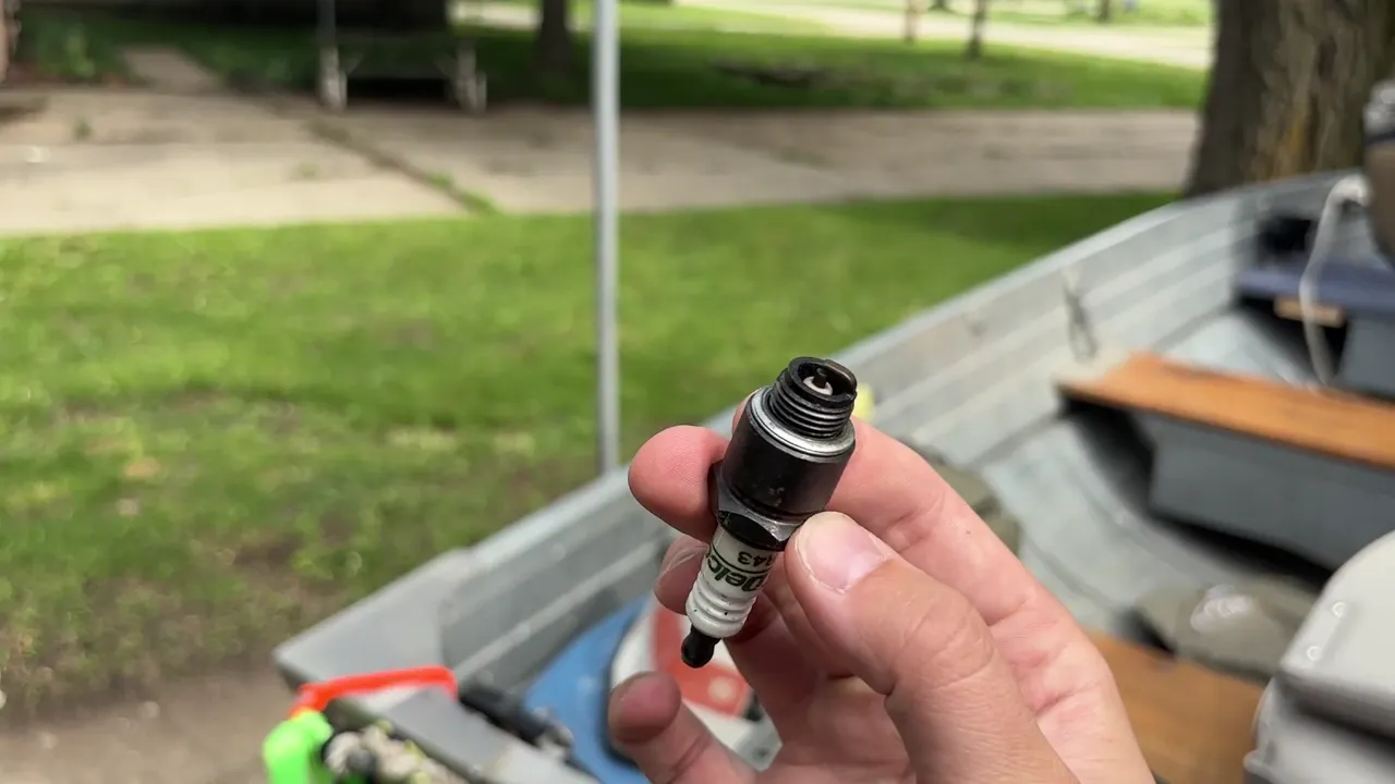 Holding a spark plug pulled from a used outboard motor